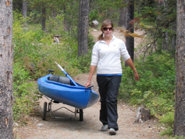 Alanna Klassen portaging kayak: girl pulling a kayak on a wheeled trailer on a forested trail