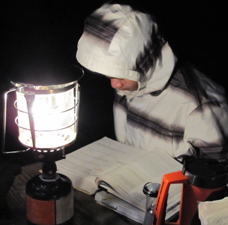 Jonathan Mai studies while camping 225 pixels: sitting at a picnic table reading by lantern light