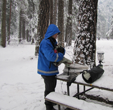 Quang packing up at end of winter 2011 trip: guy with gear on snow covered picnic table
