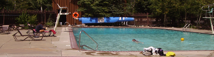 national park pool 2010: one lap swimmer and the only lifeguard on duty sitting in a lounge chair at poolside reading a book with her rescue tube drapped across the end of the lounge chair