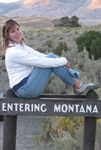 Alanna Klassen on Montana sign photo by mark Nevill: girl sitting on top of a wooden sign that says Entering montana