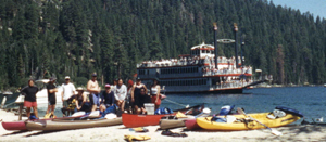 em bay kayaks: In the foreground, club kayaks and kayakers on beach at Emerald Bay. In the background, paddlewheel tourboat on the water.