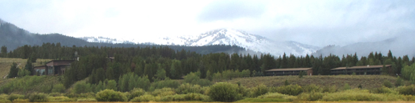 Jackson lake lodge as seen from inner park road: snow capped mountains and clouds in background, forested low hill with two large buildings