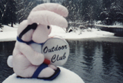 club bunny in snow: a stuffed rabbit sitting on a snowbank, banging a drum that says Outdoor Club