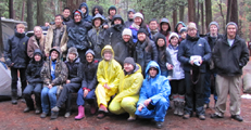 group photo 2014 Yosemite winter trip: 30 people in rain gear sitting or standing on a picnic table in a Yosemite campsite