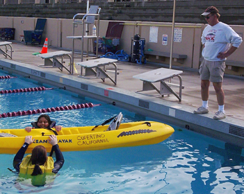 photo by Guru Parab Alan Ahlstrand watches two kayakers practice getting back into a kayak: lifeguard on pool deck watches two kayakers in the water on either side of a kayak just before they try to climb back into the kayak