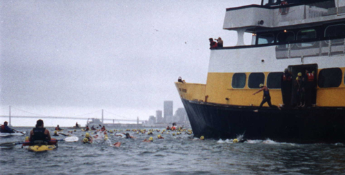 sharkfest: swimmer jumping off the ferry with the City skyline in the background and a kayak escort to the left