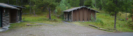 two colter bay cabins: two wood cabins and a large gravel parking area