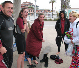 I'm going to fit my whole body in that hole: five waterfront lifeguard candidates laughing over fitting into a wetsuit, one saying "I'm going to fit my whole body in that hole" (at the neck in the top of the wetsuit)