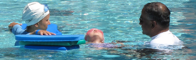 Mila and Kanishka De Lanerole assist swimmer at. the Silicon Valley Kids Triathlon 2012: two adults walk next to a 4 year old triathlete doing backstroke