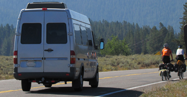 cyclists on road with narrow shoulder.: cyclists on road with narrow shoulder as a mini van approaches