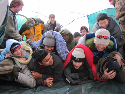 forming the group in the tent photo 2010: campers in sleeping bags setting themselves into a pile for a photo of 12 people in an eight person tent, laughing at jokes about who is on top