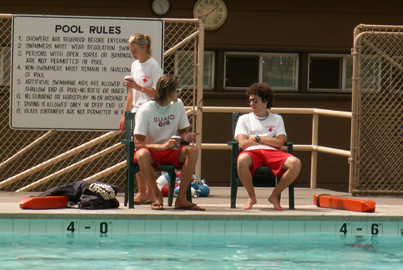 lifeguards talking with each other while on duty: two lifeguards sitting in deck level chairs with their rescue tubes on the ground, talking with each other while on duty