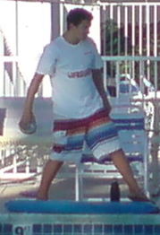 lifeguard tossing football: A lifeguard on duty at a pool tossing a football. His rescue tube is on the ground in front of him.