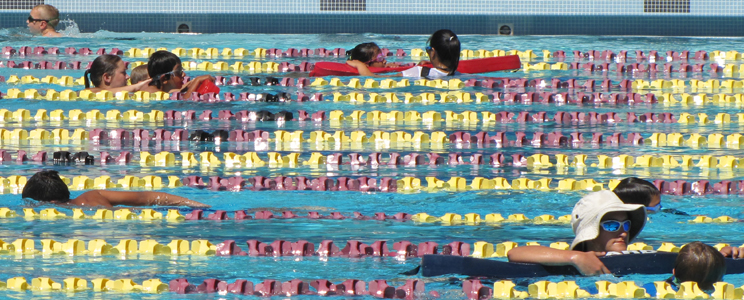 three lifeguards assist four swimmers at triathlon: struggling swimmers hold on to lifeguard rescue tubes at a traithlon, one guard has two athletes on her rescue tube