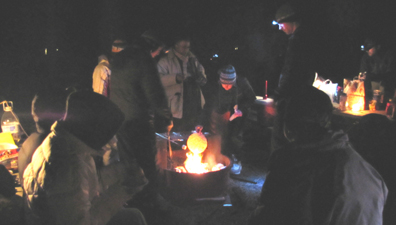 warming a tortilla at a campfire: People at picnic tables and around campfire. One is roasting a marshmallow, another is holding a tortilla over the flames.