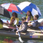 three kayaks, girls in the front holding large umbrellas, guys in the back paddling