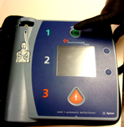 gloved finger poised over AED on off button