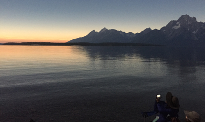 Teton range with pink sky during solar eclipse totality, person in foreground taking a picture