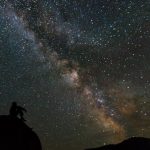 man sitting on low hill, night sky with many stars