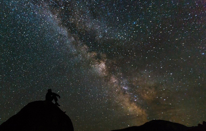 man sitting on low hill, night sky with many stars