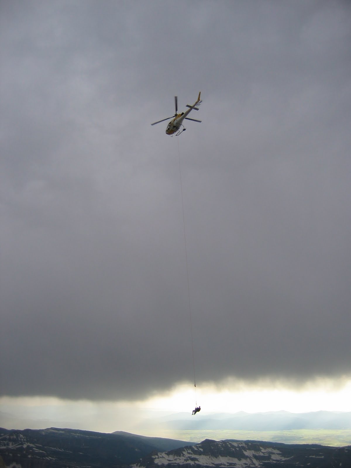 gray clouds persons hanging from helicopter