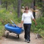 woman pulling a kayak along a trail with a trailer under it
