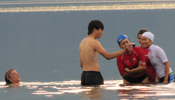 five people in lake, 2 wearing swim caps