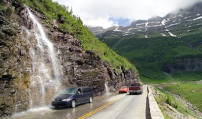car on road being sprayed by waterfall