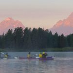 kayakers on river with mountains pink with sunrise