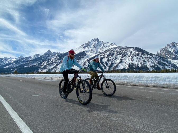 two cyclists on road with snow all around
