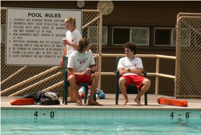 lifeguards sitting in deck level chairs with their rescue tubes on the ground, talking with each other 