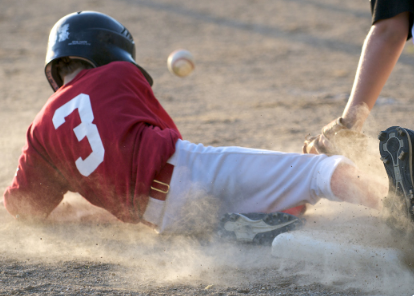 batter sliding into base with a ball in the air near his head