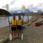 two women holding paddles standing on a river shoreline