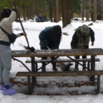 people shoveling snow off a picnic table