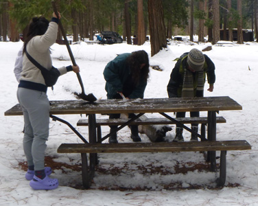 people shoveling snow off a picnic table