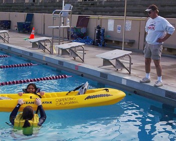 man on pool deck and two women holding sides of kayak in pool