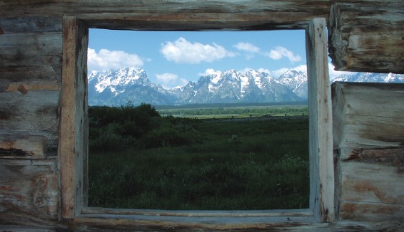 view of mountains thru window space in a log cabin