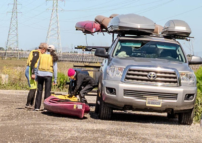 people next to kayak on ground next to trailer