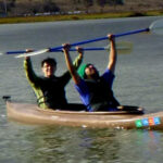 2 kayakers with their paddles raised overhead