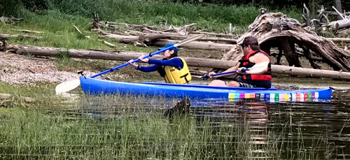 woman in kayak pushes paddle into sand bar to move kayak