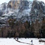 waterfall on cliff above people on boardwalk in snowy meadow