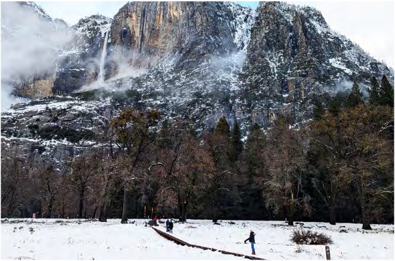 waterfall on cliff above people on boardwalk in snowy meadow