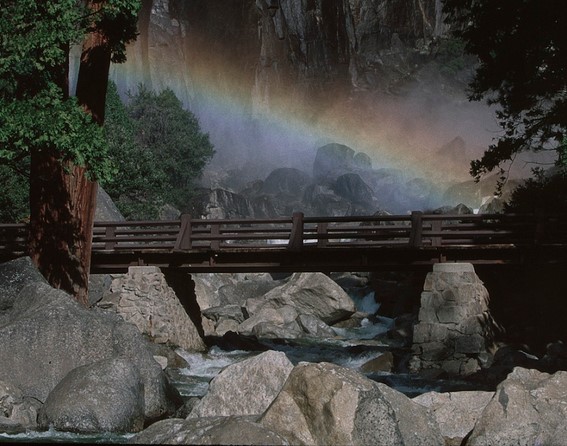 rainbow in waterfall behind footbridge