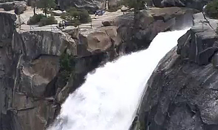 people standing near railing at cliff over waterfall