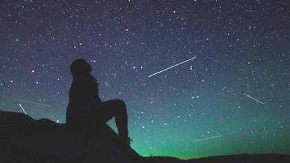 shooting stars beyond silhouette of seated person