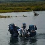 three backpackers wading across a river next to each other