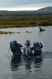 three backpackers wading across a river next to each other