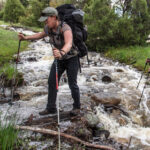 two adults wearing packs crossing a stream