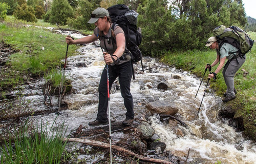 two adults wearing packs crossing a stream